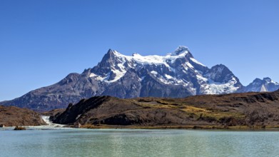 Snowy mountain above a calm river and turquoise water under a blue sky, The landscape of the Torres
