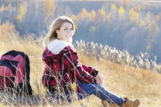 Young happy woman having fun outdoors sitting on the top of the hill. Backpacking tourism concept
