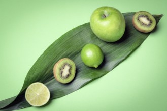 Mix of raw fruits on a green leave. Green kitchen table with fresh detox fruits