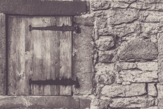Architectural frame with a weathered wooden trap door and the stone wall, from a traditional german