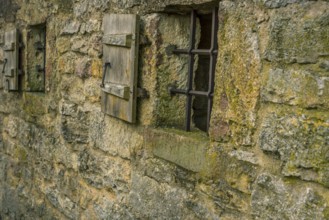 Medieval stone wall with two small windows, fortified with metal bars