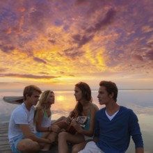 Friends young group at sunset beach having fun playing guitar in pier