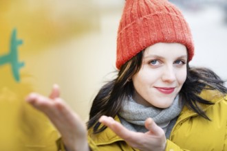 Woman with red hat and yellow jacket gestures to electric car for transport against urban