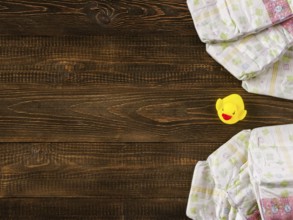 Japanese disposable diapers and the rubber duckling on dark wooden background with copy-space. Flat