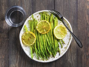 Grilled asparagus and slice of lemon in craft trendy plate on dark brown wooden table. Top view or