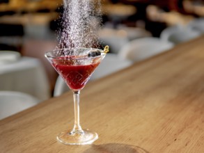 Red cocktail in martini glass on bar counter. White powdered sugar sprinkled on alcohol cocktail