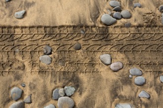 Car tire footprint in a sand and rolling stones beach texture