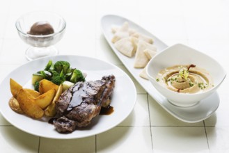 Grilled steak meal with hummus dip starter on table