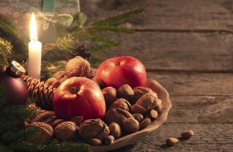 Christmas scenery with a wooden platter full of walnuts, hazelnuts and apples, green fir twigs and