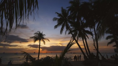Silhouetted people and palms near sea. Sunset at tropical White beach, Boracay island, Philippines,