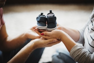 Young future parents holding baby booties shoes in their hands