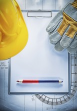 Clipboard pencil building helmet safety gloves on blueprint construction concept