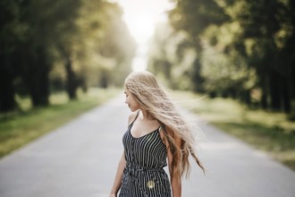 Woman facing sideways on a quiet road, her long hair flowing, creating a thoughtful and solitary