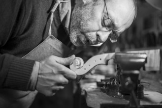 Intense concentration of a craftsman chiseling a spiral intoa violin scroll