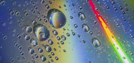 Beautiful closeup of water droplets floating on blueish silver background with rainbow colors