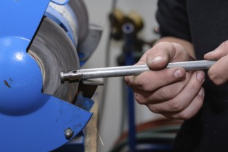 Skilled worker working on metal on a bench grinder - close-up
