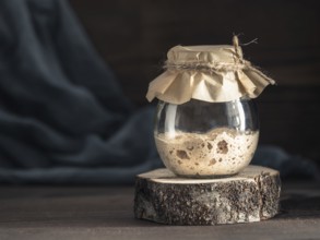 Active rye sourdough starter in glass jar on brown wooden background. Starter for sourdough bread.