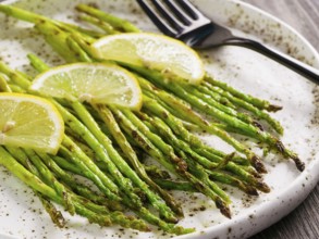 Close up view of grilled asparagus and slice of lemon in craft trendy plate on brown wooden table