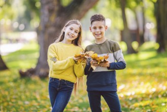 Happy twins teenagers boy and girl posing hugging each other in autumn park holding fallen yellow