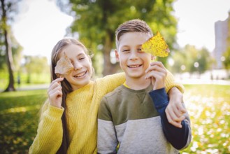 Happy twins teenagers boy and girl posing hugging each other in autumn park holding fallen yellow