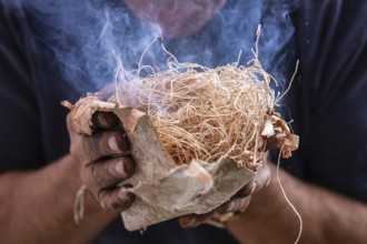Closeup of man hand holding straw used as fire starter with smoke during demonstration of native