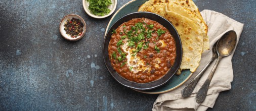 Traditional Indian Punjabi dish Dal makhani with lentils and beans in black bowl served with naan