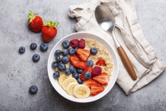 Oatmeal porridge with fruit and berries in bowl with spoon on white wooden background table top