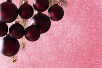 Elegant dark red Christmas balls hanging while snowing, from a snow spray, in bright light, perfect