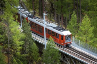 Zermatt, Switzerland, October 7, 2019: Gornergrat red tourist train on the bridge, village houses