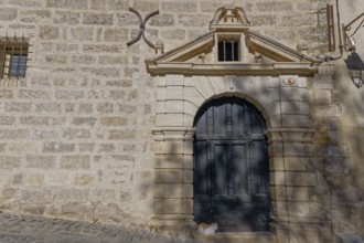 An old architectural stone wall with an ornate door casting shadows and a cat in the gentle warmth