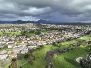 Aerial view of residential neighborhood surrounded by golf and valley during cloudy day in Rancho