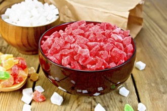 Candied papaya and coconut in bowls, colorful pieces of candied fruit in a spoon on a wooden boards