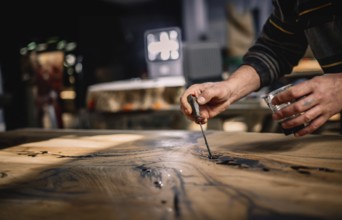 Close-up of hands expertly applying a tool to a wood surface under warm lighting in a shop setting