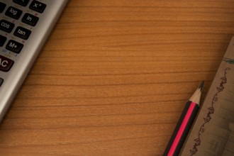 Wooden table with calculator in one corner and pencil and notebook in another