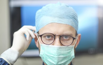 A surgeon wearing glasses and a mask with a focused expression