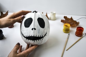 Woman paints face on orange pumpkin for Halloween. Autumn leaves. Diy children craft. Do it