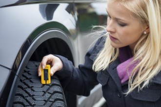 A young woman measures the tread depth of her car tyre. The right depth in the tread of a tyre can