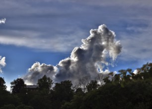 Threatening thundercloud grows behind a house into the blue sky, dramatic cloud formation, Upper