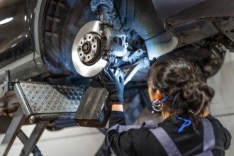 Female mechanic working under a car, inspecting and repairing brakes in a professional workshop