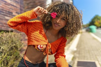 Latin beauty woman flirting and playing with heart shaped lollipop sitting outside a house in the