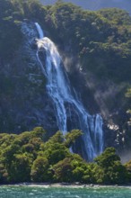 Waterfall cascades over a wooded slope and sprays fine spray into turquoise-coloured water, summer,