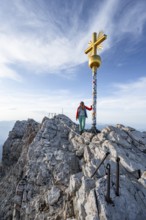 Mountaineer in front of golden summit cross, summit of the Zugspitze, Wetterstein range, Bavaria,