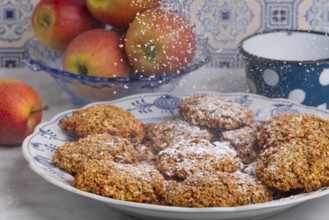 Freshly baked oat biscuits on a plate are sprinkled with sugar, apples in the background