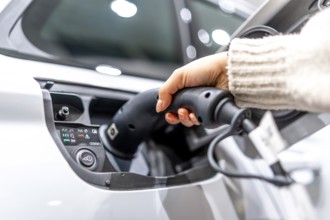 Close up of a hand plugging a charging cable into an electric vehicle at a car dealership,