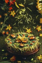 Easter grass falls on Easter cake with carrots and chocolate eggs surrounded by flowers in green