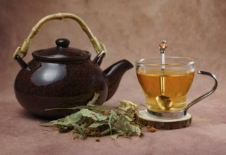 Glass cup with teapot and fresh linden leaves, infusion of lime blossom tea, medicinal plant with