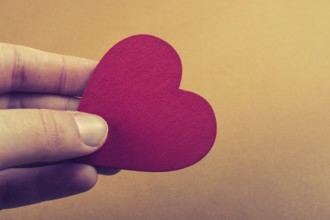 Red color heart shaped object in hand on dotted paper