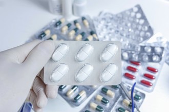A gloved hand holding a blister pack of white pills amidst various capsules