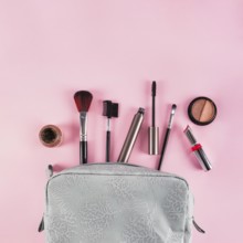 Makeup products spilling out bag pink background