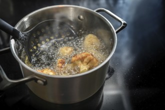 Deep frying cauliflower florets in a pot with boiling cooking oil on the stove, preparation of a
